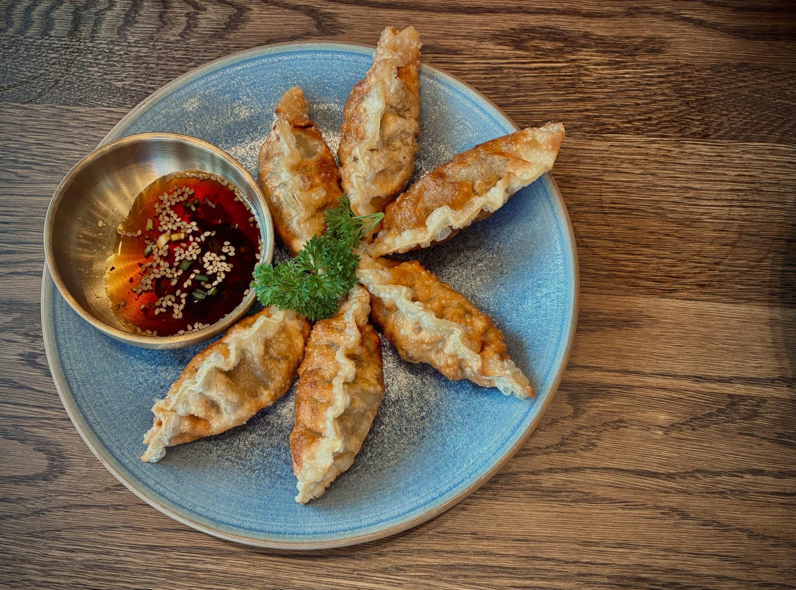 Crispy fried dumplings served with soy and sesame dip on a blue plate.